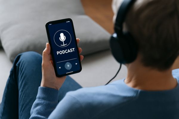 Pessoa adulta ouvindo podcast com fones de ouvido no celular